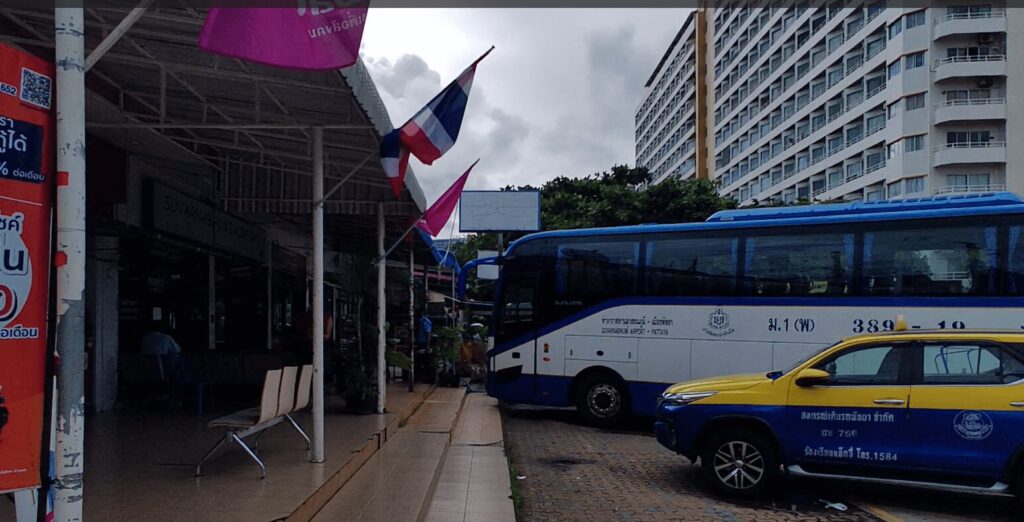 A Roong Reuang Coach bus parked at the Jomtien Bus Terminal, with passengers and waiting area visible