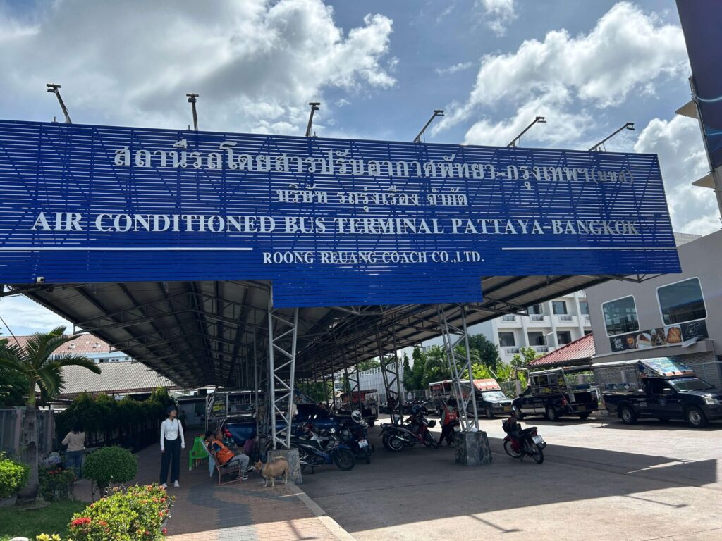 Large blue sign for "AIR CONDITIONED BUS TERMINAL PATTAYA-BANGKOK" at the entrance of North Pattaya Bus Terminal, with cars and motorbikes.