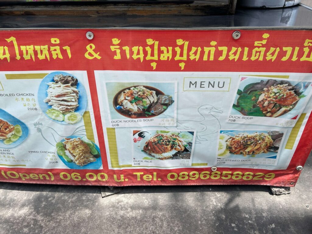 Menu sign at a Thai street food stall showing various duck dishes with prices in Thai Baht