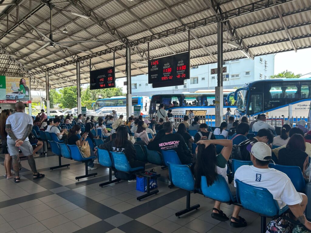 Passengers waiting in the covered seating area at North Pattaya Bus Terminal, with buses parked at the bays.