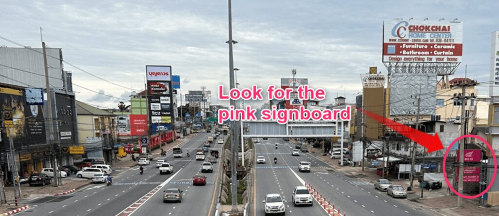 A large pink signboard on the roadside, serving as a landmark for locating the Bor Kor Sor bus station in Pattaya for buses to Don Mueang, Suvarnabhumi Airport