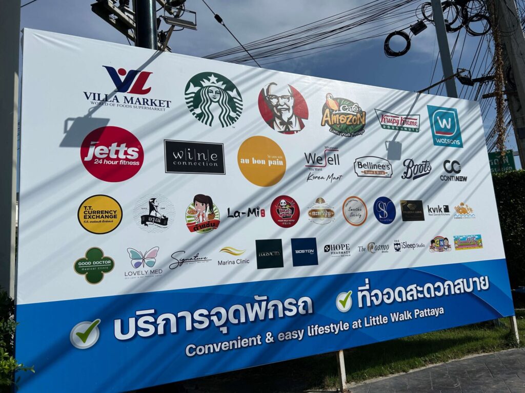 A directory board at Little Walk Pattaya showcasing logos of various popular tenants including Villa Market, Starbucks, Jetts Fitness, and Krispy Kreme, highlighting essential services and diverse shopping options for bus travelers.