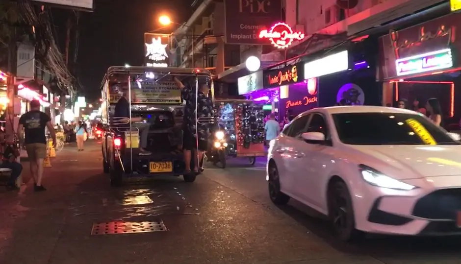 A blue songthaew traveling along Soi Buakhao in Pattaya. The street is busy with other vehicles, people walking, and a variety of small shops and signs lining the road