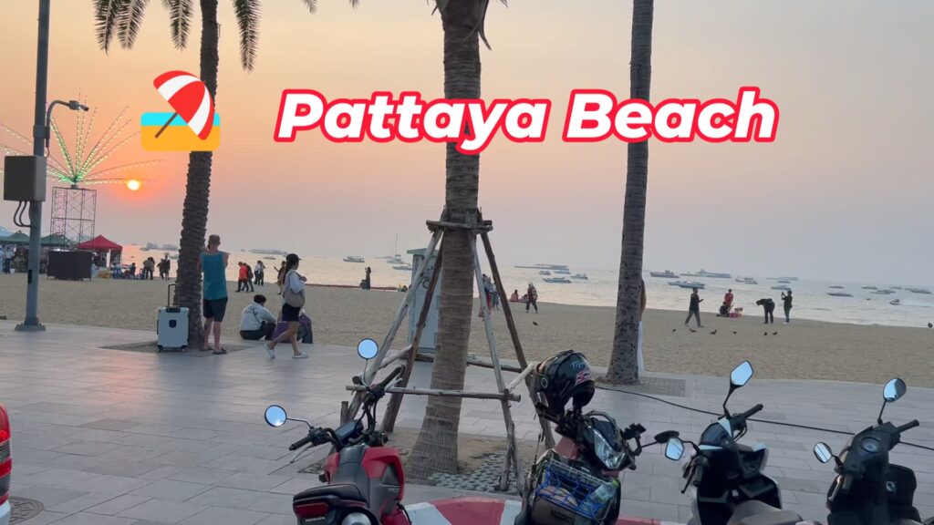 A beautiful sunset at Pattaya Beach, with the sun setting over the ocean. Palm trees and parked scooters line the beach promenade, and tourists are seen enjoying the view.