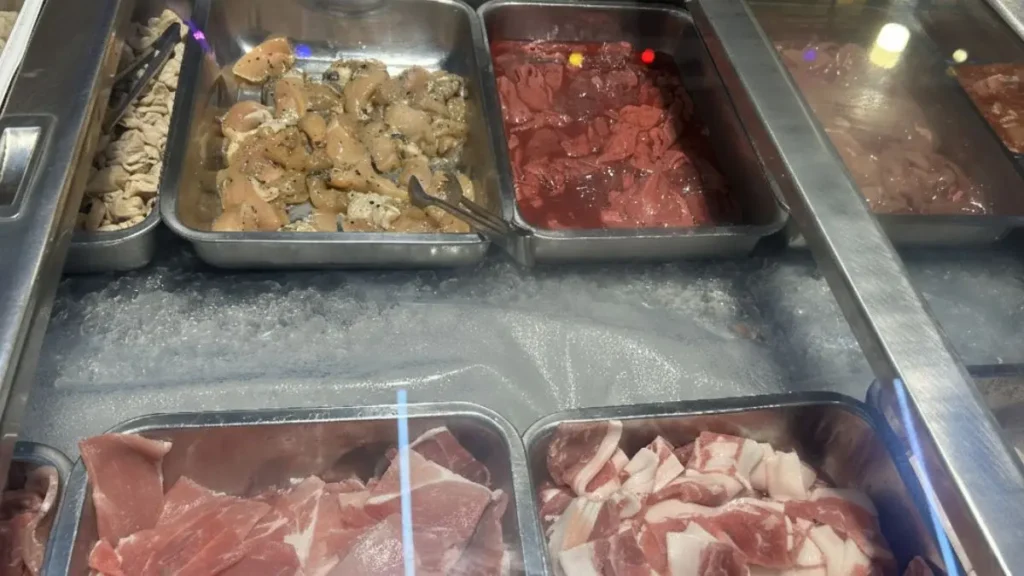 A refrigerated display of fresh mookata ingredients, including marinated meats, ready for grilling at the Phaa Nong Mookata (ป๋าหน่อง).