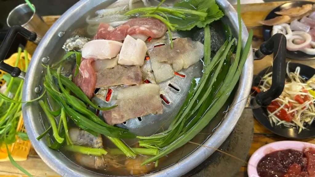 A close-up view of meat and vegetables actively cooking on the mookata grill at Phaa Nong (ป๋าหน่อง) restaurant.
