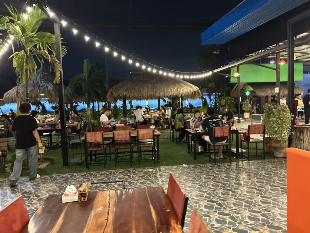 The lively outdoor seating area at Ruam Phuean at night, illuminated by warm string lights and surrounded by palm trees.
