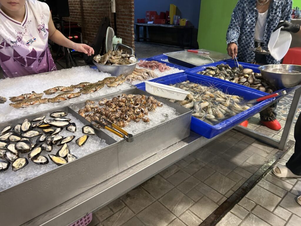 A close-up view of the fresh seafood section on ice, including clams, mussels, shrimp, and crab ready for grilling.