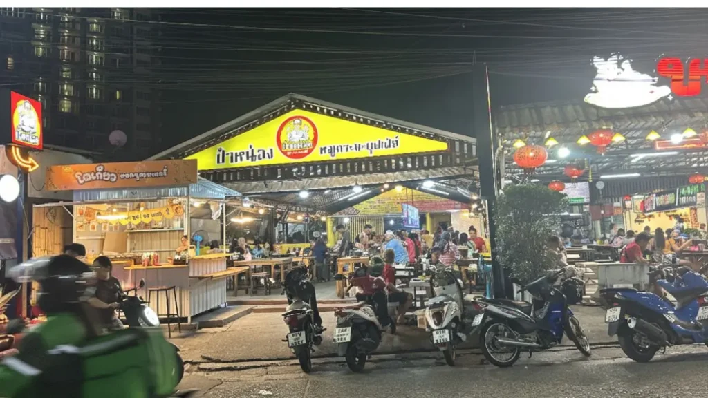 The illuminated exterior of the busy Pattaya Mookata restaurant, Phaa Nong (ป๋าหน่อง หมูกระทะบุฟเฟ่ต์) at night, with motorbikes parked outside.