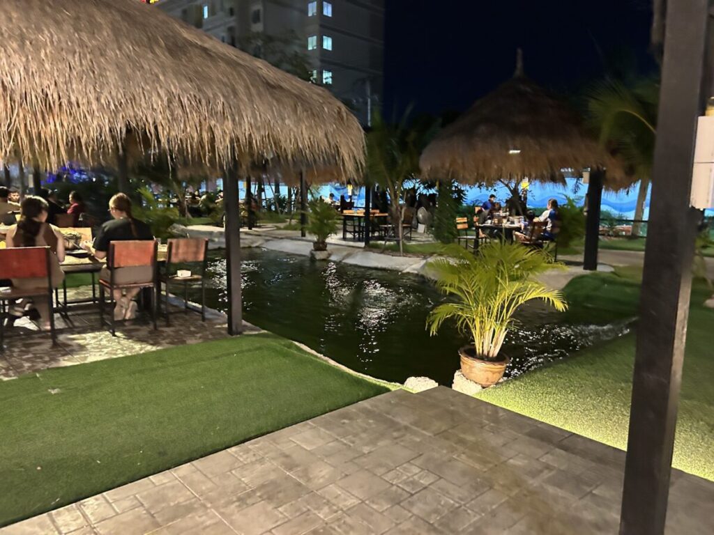 Customers dining in straw-roof huts next to the tranquil decorative pond at Ruam Phuean Mookata in Pattaya.