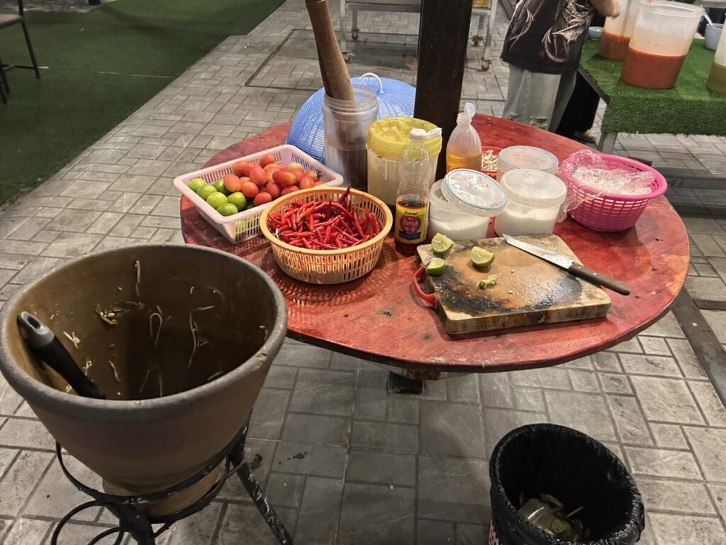 The self-service Som Tam (papaya salad) station featuring fresh ingredients like chilies, limes, tomatoes, and the pestle.