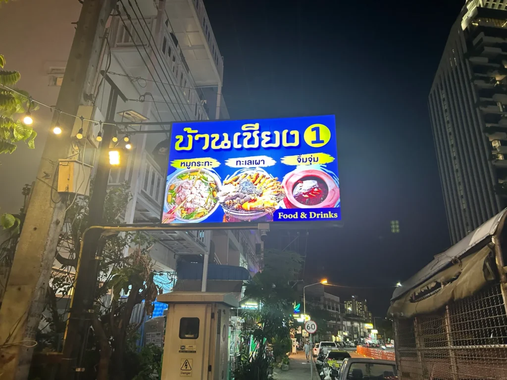 Brightly lit outdoor sign for "Ban Chieng 1 Mookata" on Third Road, Pattaya, showing images of Thai BBQ, seafood, and hot pot at night.