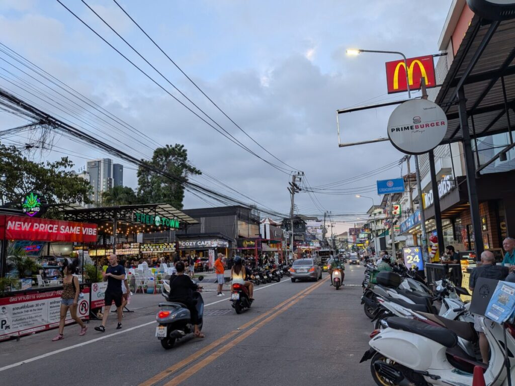 The bustling daytime street scene on Soi Buakhao near the Tree Town area, showing local vendors, affordable food stalls, and traffic.