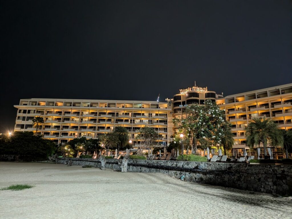 A view of the upscale Dusit Thani Pattaya exterior at night, showing the hotel's prominent location near the ocean and the lit surrounding area.