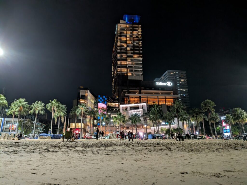 The vibrant night view of Pattaya Beach Road with brightly lit hotels, street lights reflecting on the wet road, and the lively atmosphere.