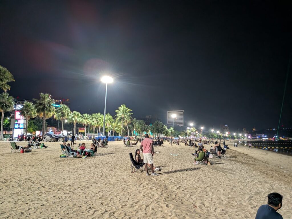 The vibrant night scene on Pattaya Beach Road, featuring brightly lit palm trees, streetlights, and people enjoying the evening near the hotel area.