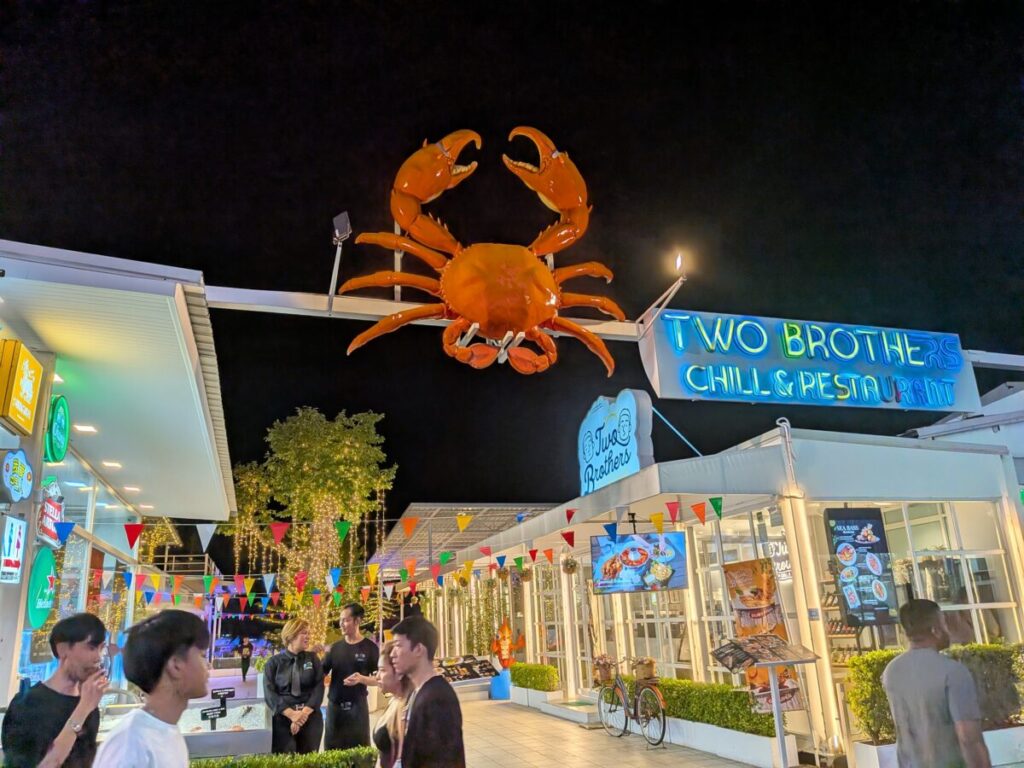 An atmospheric night view of the South Pattaya beach road area, featuring small open-air bars, street vendors, and lively night time crowds.