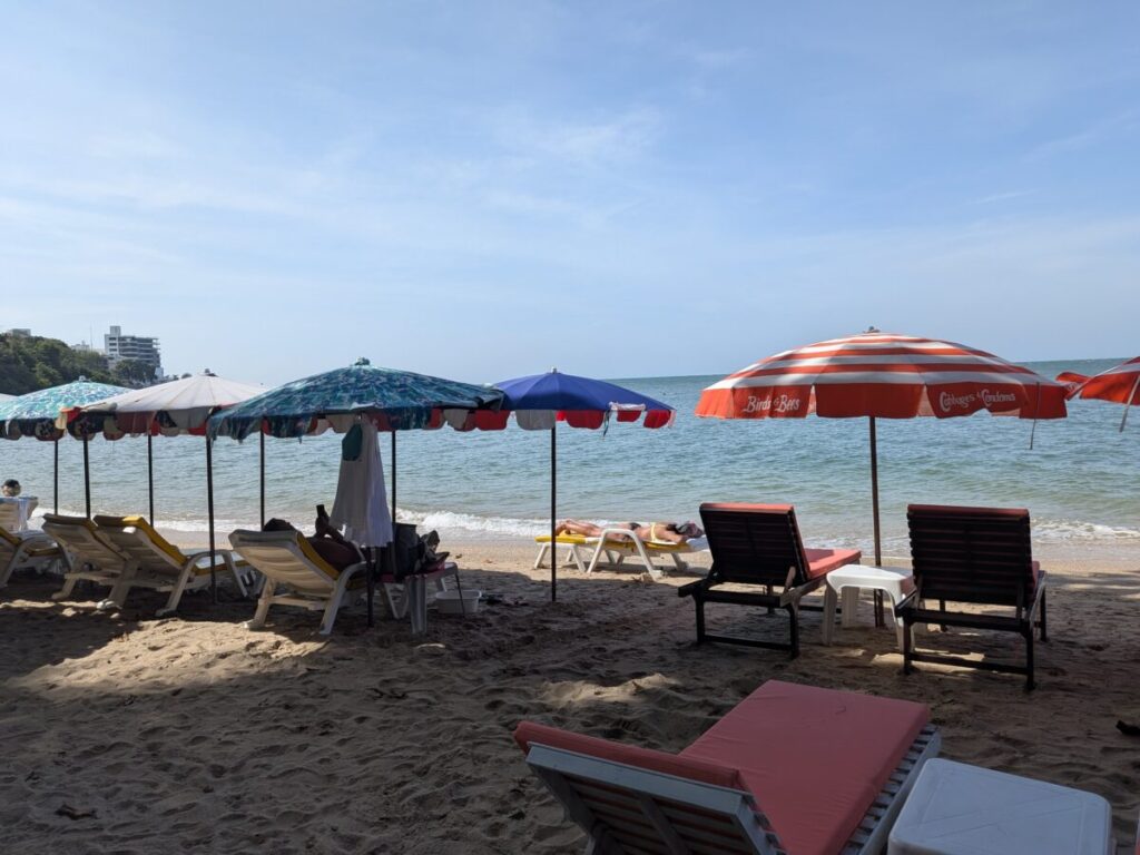 Colorful beach umbrellas and chairs lined up on Paradise Beach Pattaya with calm waves in the background
