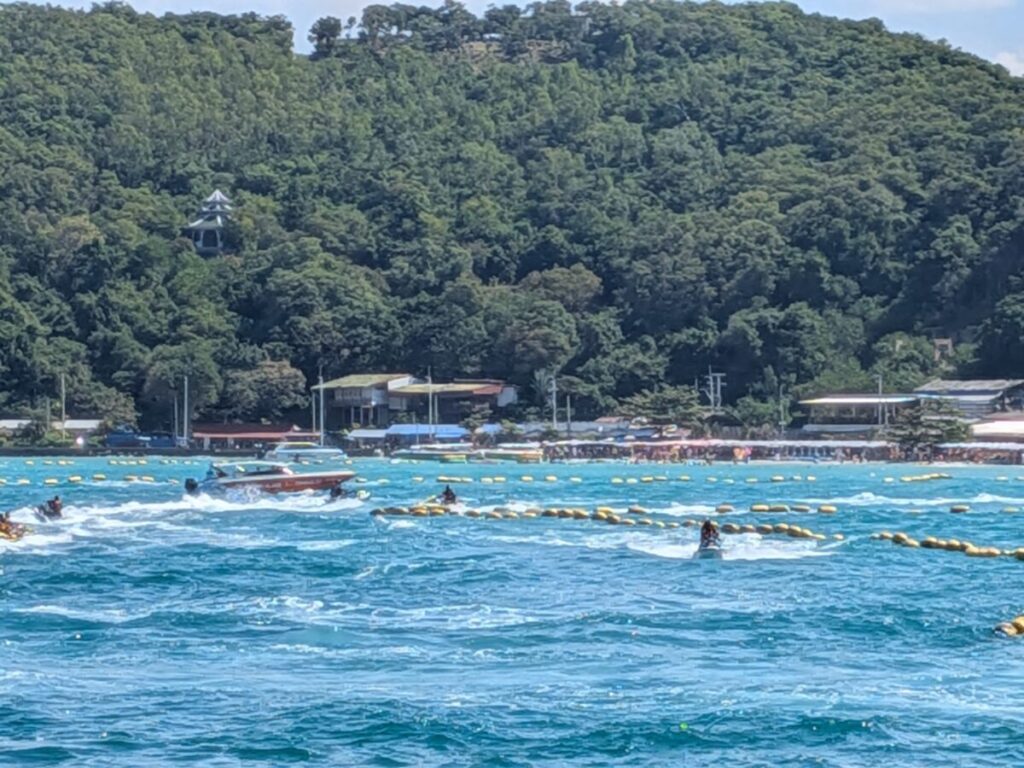 Ocean view at Tawaen Beach with speedboats, turquoise water, and the hillside pavilion in the background.