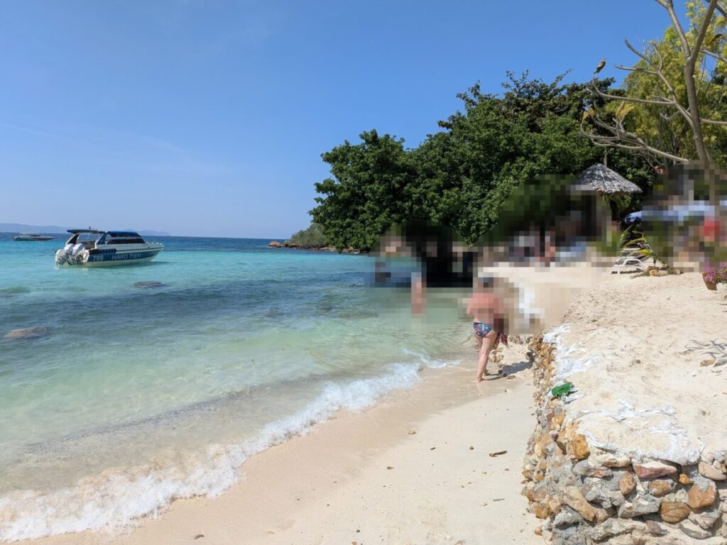 A calm shoreline at Tien Beach with clear turquoise water, a speedboat anchored offshore, and beachgoers relaxing by the sand.