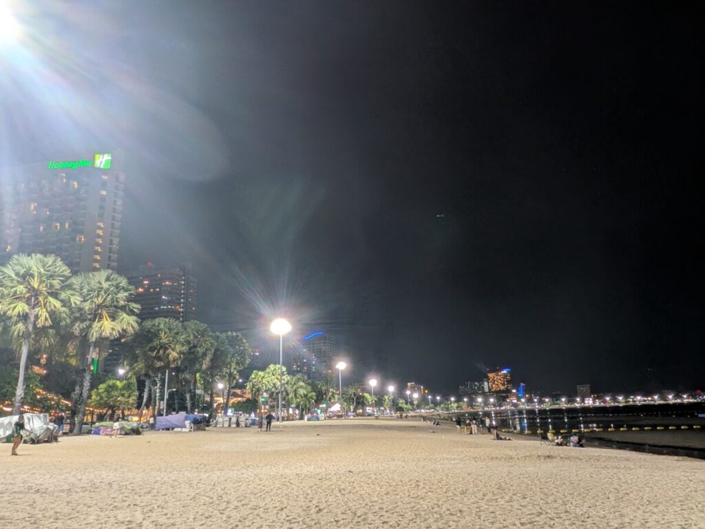 Night view of Pattaya Beach Road with streetlights along the sandy beach and a few visitors walking nearby