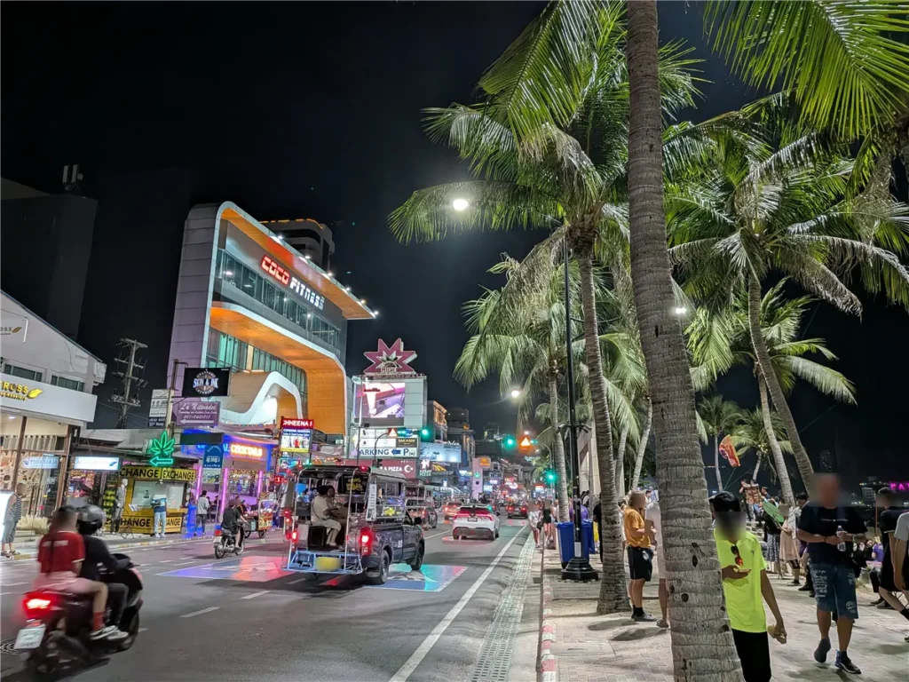 Pattaya Beach Road at night with palm trees, traffic, and illuminated shops