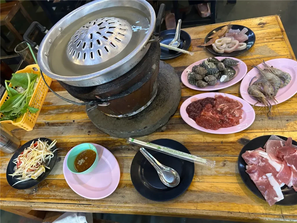 Mookata pan with meat grilling on the raised dome and ingredients cooking in the surrounding broth